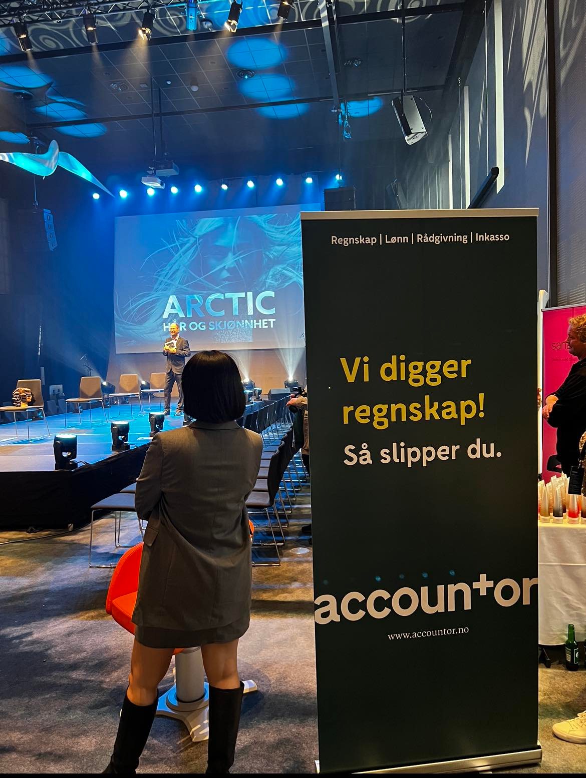 Dame som står ved siden av accountor skilt foran scene i Bodø frisørsamling