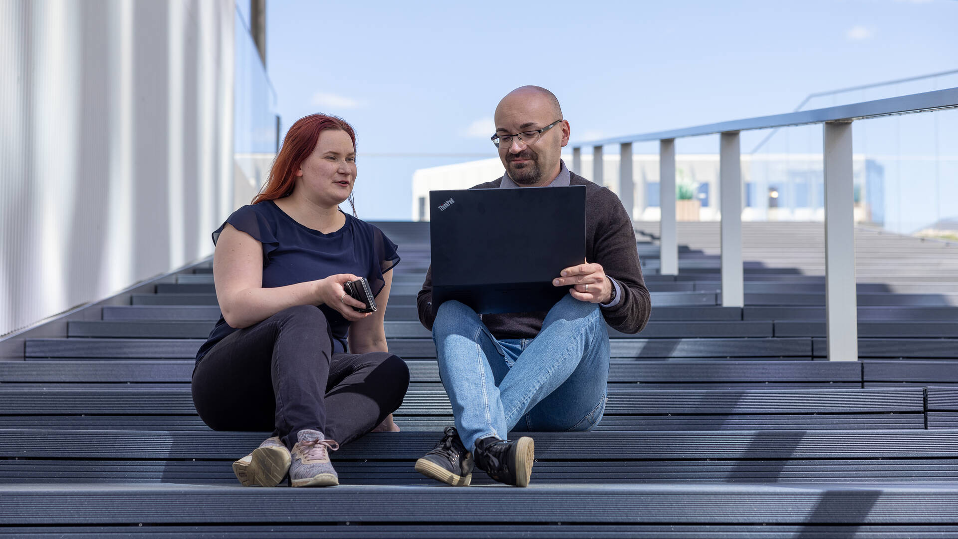 Woman and man sitting on stairs outside with laptop