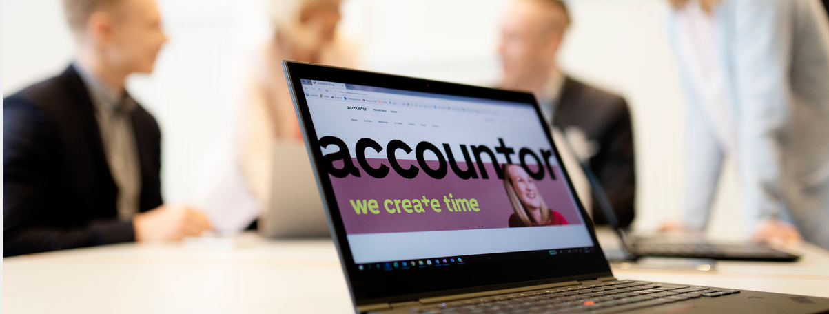 En pc i et rom med masse mennesker, pcen står i fokus med teksten "we create time" på skjermen