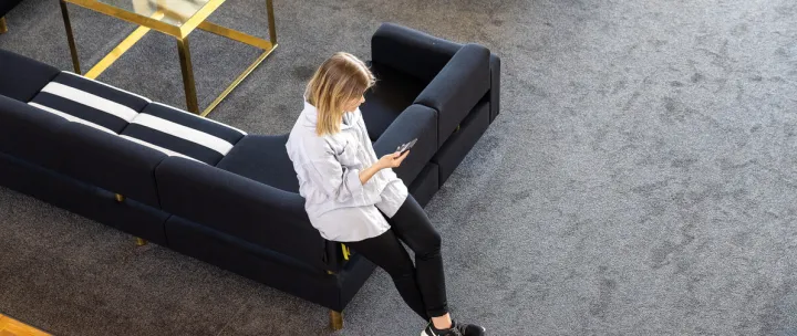 Mari som lener seg mot en sofa og ser på telefonen i fellesarealet