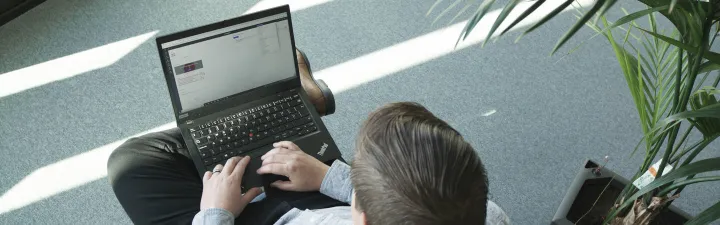 Mann med pc sitter i en stol med en plante på høyre side