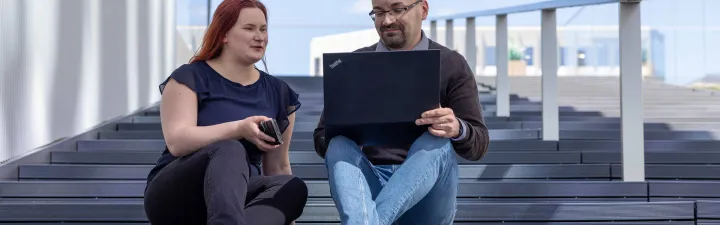 Woman and man sitting on stairs outside with laptop