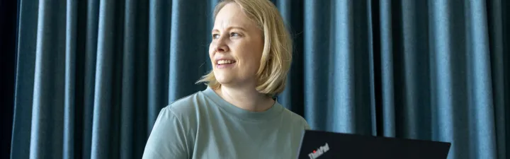 kvinne med laptop foran en blågrønn vegg