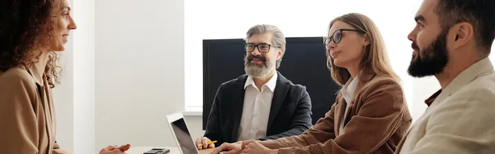 Flere sitter rundt et bord i en intervju prosess. det er en kvinne som blir intervjuet 