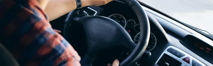 Person om kjører bil. Du ser personen bakfra ifra fugleperspektiv ned på rattet.