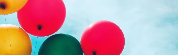 Ballonger i gult, grønt og rødt som svever oppp mot en blå himmel med litt skyer 