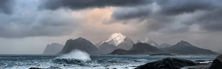 Sjøen som slår imot steinene med fjellene i bakgrunnen